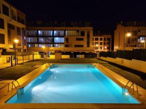 a large blue swimming pool at night with buildings at Gestiona2R - Apartamento para 2 con piscina in Posada de Llanes