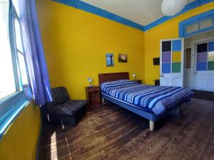 a yellow bedroom with a bed and a chair at Casaclub Hostel in Valparaíso