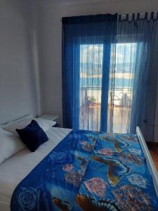 a bed with a blue comforter and a window at Apartmani Vesna in Pag