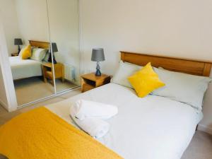 a bedroom with a white bed with yellow pillows and a mirror at Brand new gorgeous 2 bed Apt in Finnieston in Glasgow
