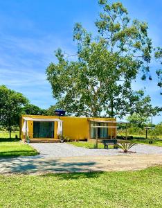 uma casa amarela com um banco num parque em Container Suítes Recanto Monte Trigo em São Francisco do Sul