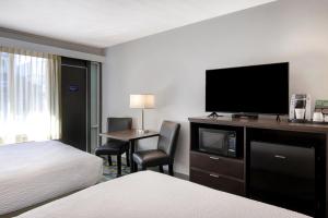 a hotel room with a bed and a desk with a television at Days Inn by Wyndham Victoria Airport Sidney in Sidney