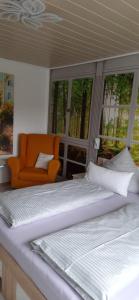 2 Betten in einem Zimmer mit orangefarbenem Stuhl und Fenstern in der Unterkunft Der Frühe Vogel in Plaue