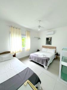 a white room with two beds and a window at Pousada Village Cozumel in Guarujá