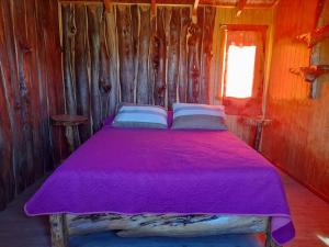 Cama en habitación de madera con sábanas y almohadas moradas en Cabaña El artesano Puyehue en Ñilque
