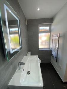 a bathroom with a white sink and two windows at NEW! Brand New Beautiful Modern Apartment in London