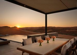 a table and chairs with a sunset in the desert at The Ritz-Carlton Ras Al Khaimah, Al Wadi Desert in Ras al Khaimah