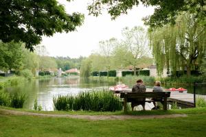 dos personas sentadas en un banco junto a un lago en Glamping Limburg en Oostrum
