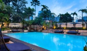 a large blue swimming pool with palm trees and umbrellas at Sari Pacific Jakarta, Autograph Collection in Jakarta