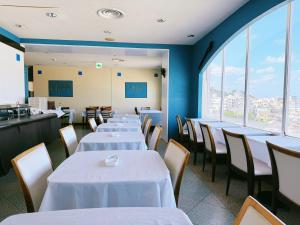 un comedor con mesas y sillas blancas y ventanas en Hotel Orox, en Naha