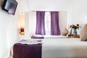 a bedroom with two beds and a window with purple curtains at Lancaster Court Hotel in London