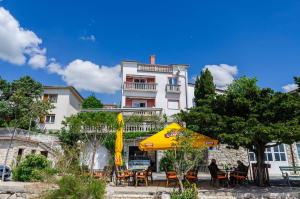 a building with tables and chairs and a yellow umbrella at Balkon mit Meerblick direkt am Strand in Jadranovo