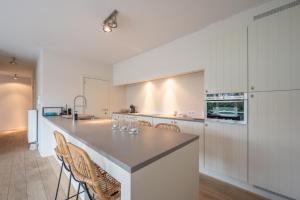 una cucina con armadi bianchi e bancone con sedie di Beautiful beach-appartment between Knokke & Bruges a Zeebrugge