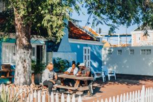 four people sitting around a picnic table in front of a blue building at The Freedom Hotel in Willemstad