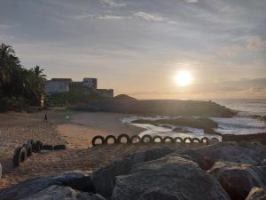 una playa con rocas y el sol saliendo sobre el océano en Orange Beach hostel, en Cape Coast
