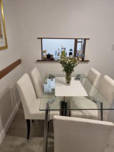 Elegante 3 dormitorios في بوينس آيرس: طاولة زجاجية مع كراسي بيضاء و مزهرية من الزهور