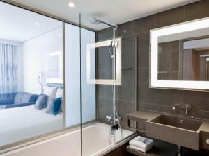 a bathroom with a shower and a sink and a bed at Novotel Lugano Paradiso in Lugano