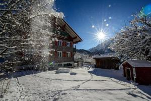 a building covered in snow with the sun behind it at Alpakahof Wechs in Bad Hindelang
