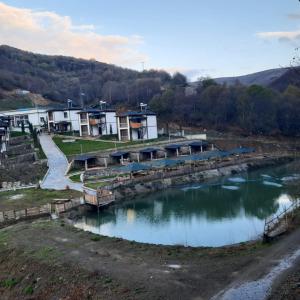 un río con un grupo de edificios en el fondo en Yeşilgöl doğa evleri, en Tokat