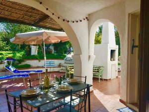 une terrasse avec une table, des chaises et un parasol dans l'établissement Villa i Ginepri. A pochi passi dal mare., à Marina di Sorso