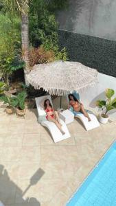 two women sitting in chairs under an umbrella next to a pool at The White Villa in Lipa in Lipa