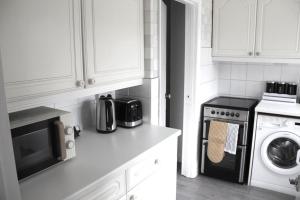 a kitchen with white cabinets and a black microwave at Coolfin House - London Excel in London