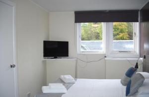 a bedroom with a bed and a tv and two windows at The Breadalbane Arms Room Only Hotel in Aberfeldy