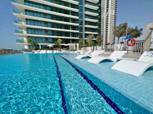 a swimming pool with white chairs and a large building at Silkhaus new 1BDR with Private beach in Dubai
