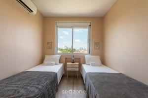 two beds in a room with a window at Confortável apto em Porto Alegre/RS PRL0602 in Porto Alegre