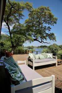 a deck with two couches and a tree and water at Zambezi Dusk in Livingstone