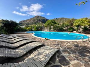 a swimming pool with benches and mountains in the background at Villa Saraceno in Lipari