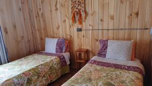 2 camas en una habitación con paredes de madera en Casa Bosque Pichilemu en Rinconada El Sauce