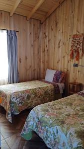2 camas en una habitación con paredes de madera en Casa Bosque Pichilemu, en Rinconada El Sauce