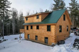 une maison en bois avec un toit vert dans la neige dans l'établissement 65PT New Log Cabin in Private Setting. Hot tub. Gym/Pool Access!, à Twin Mountain