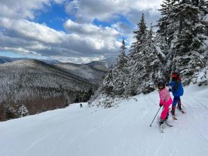 two children are skiing down a snow covered slope at 65PT New Log Cabin in Private Setting. Hot tub. Gym/Pool Access! in Twin Mountain