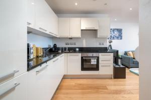 a kitchen with white cabinets and a living room at LUX CONDO for 5 Slough Elizabeth line free parking in Slough