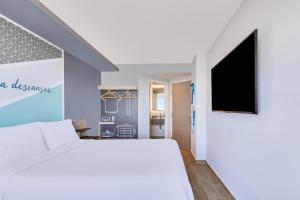 1 dormitorio con 1 cama blanca y TV de pantalla plana en One Mazatlán en Mazatlán
