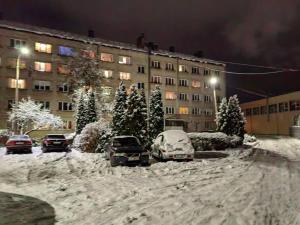 a snow covered street with cars parked in front of a building at Apartamenti dzīvoklis Ogre. in Ogre