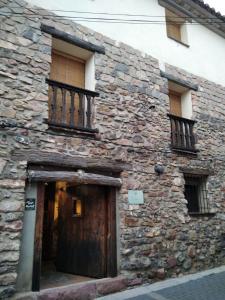 Edificio de piedra antiguo con puerta de madera y balcón en Casa la Cisterna, en Pina de Montolgrao