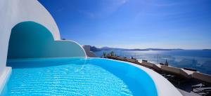 a swimming pool with chairs and the ocean in the background at Nostos Apartments in Oia