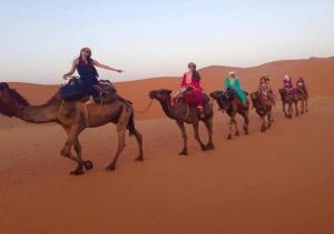 Eine Gruppe von Menschen, die auf Kamelen in der Wüste reiten in der Unterkunft Desert Season Camp in Merzouga