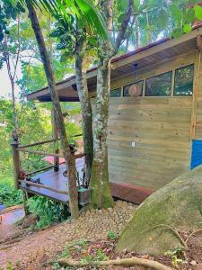 een huis met een houten veranda naast twee bomen bij Eco Cabana a 150 metros da praia e centrinho in Paraty