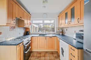 eine Küche mit Holzschränken, einem Waschbecken und einem Fenster in der Unterkunft Comfy Home Ideal for Groups - Free Parking in Bedford
