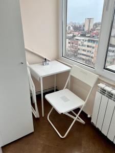 einen kleinen weißen Tisch und Stuhl in einem Zimmer mit Fenster in der Unterkunft Amy's Bright Apartment in Constanţa