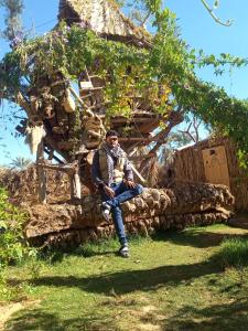 a man sitting on a stone wall in front of a tree at Five oasis desert camp in Az Zabū