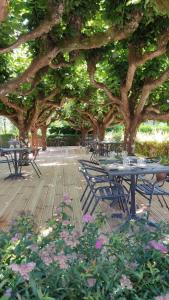 une terrasse en bois avec des tables et des chaises sous les arbres dans l'établissement Hotel de L'Hippodrome, à Arnac-Pompadour