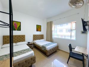 a bedroom with two beds and a desk and a window at Hotel Central Plaza Medellin in Medellín