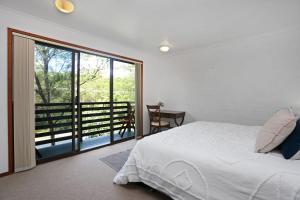 a white bedroom with a bed and a balcony at LingaLonga in Hawks Nest