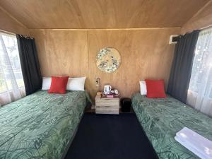 two beds in a small room with green and red pillows at Tui Lodge in Coromandel Town