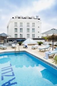 a pool with chairs and a building in the background at Hotel Mar Azul & Surf in Suances